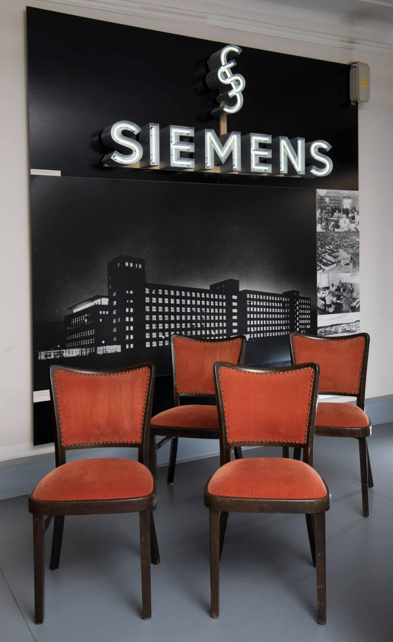 Vier rot gepolsterte Stühle aus dem Erlanger Himbeerpalast vor einem Großfoto des Gebäudes
