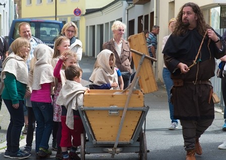 Kinder und ein Museumspädagoge in historischen Kostümen ziehen mit einem Leiterwagen durch die Stadt