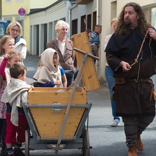 Kinder und ein Museumspädagoge in historischen Kostümen ziehen mit einem Leiterwagen durch die Stadt